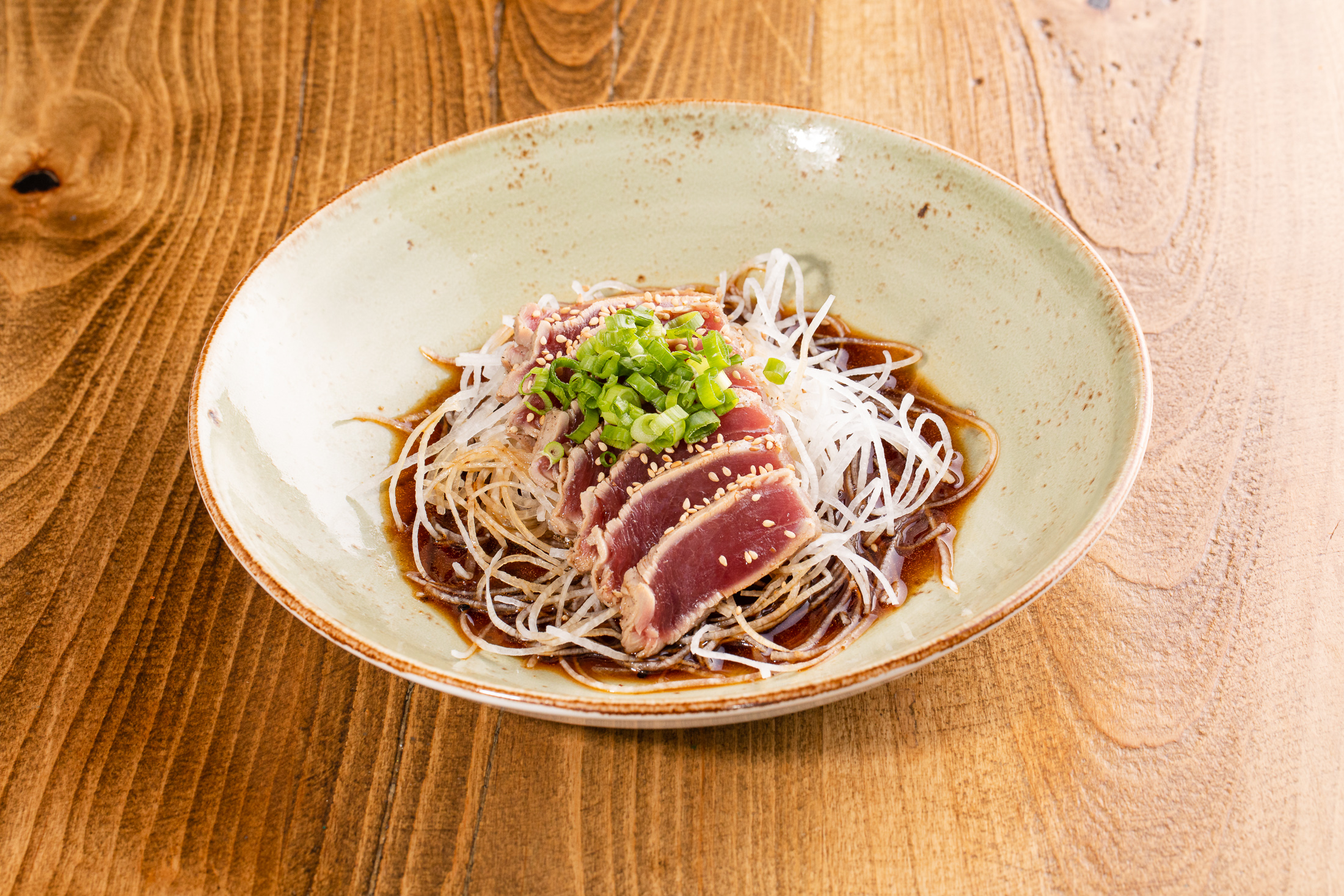 Lightly seared raw tuna in shichimi gluten-free soy dressing on top of daikon radish shoestrings with green onion, sesame seeds